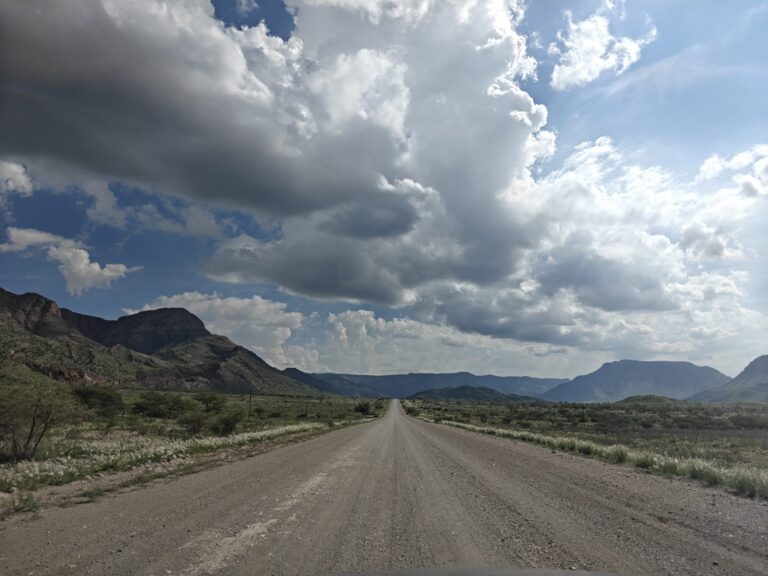 Long straight gravel road in Namibia with mountains and storm clouds