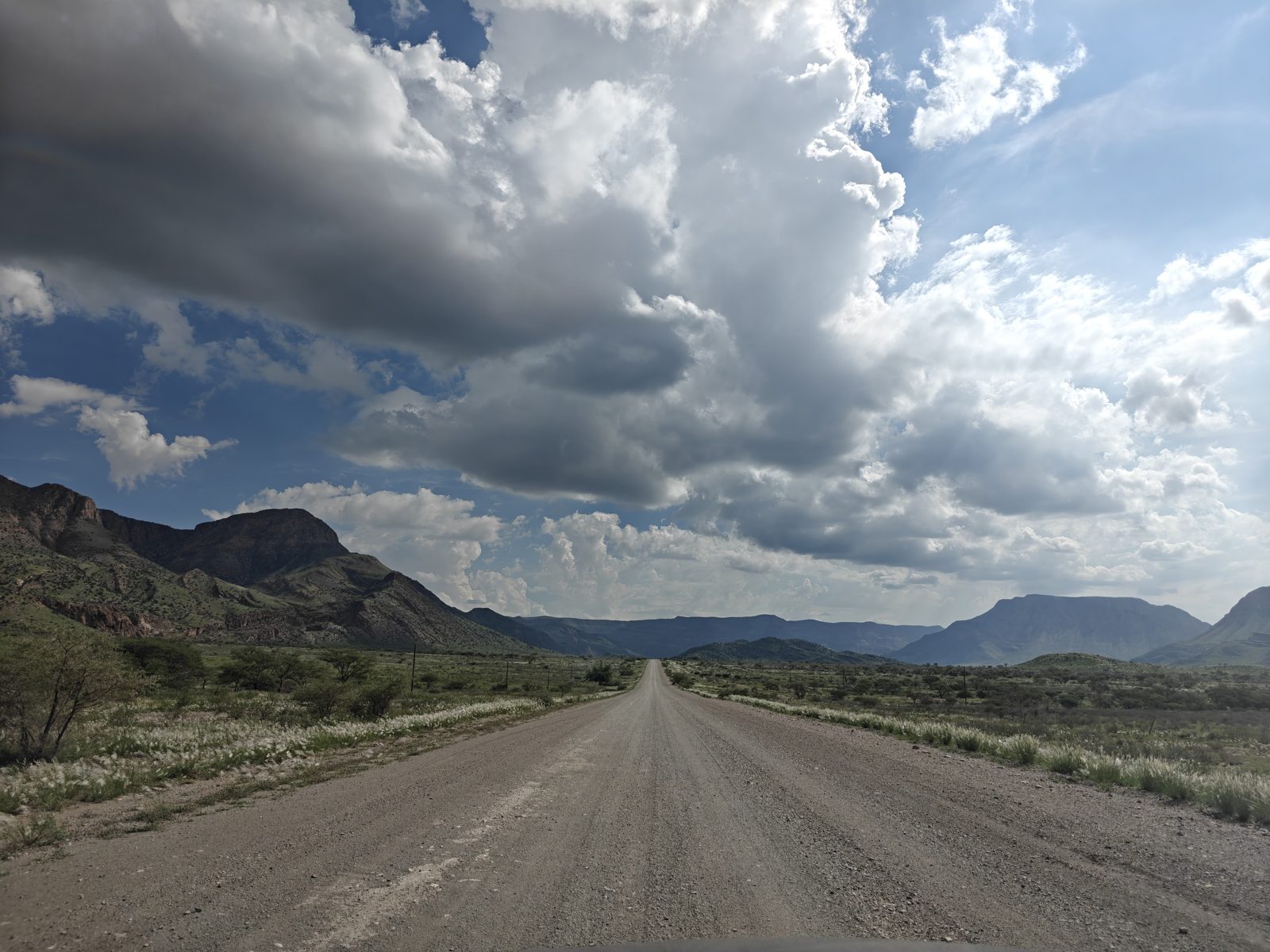 Long straight gravel road in Namibia with mountains and storm clouds